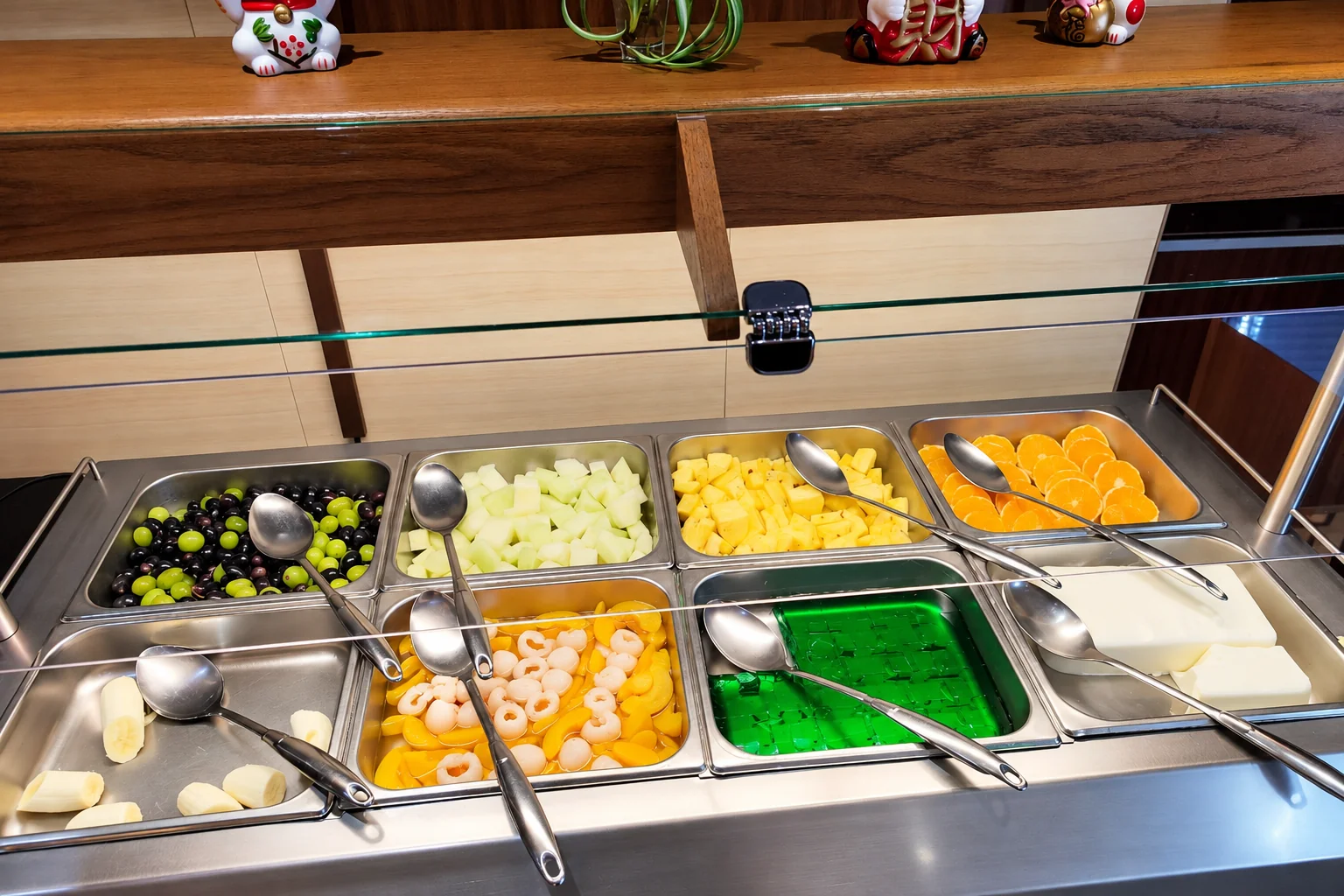 Obst und grüner Wackelpudding in Edelstahlschalen am Büffet, mit Schöpflöffeln.